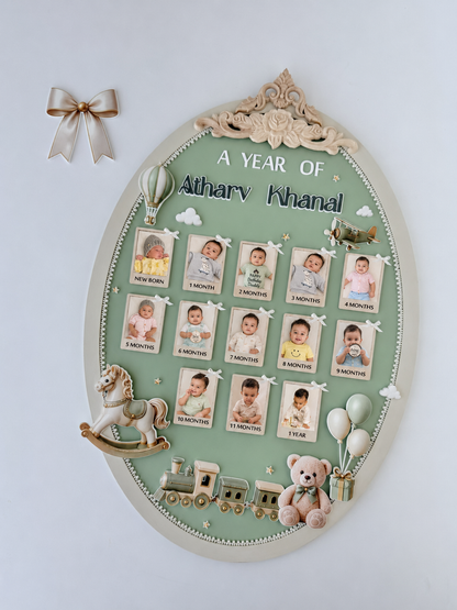 Green oval nursery milestone board with thirteen ribbon-tied photos, a rocking horse, toy train, teddy bear, and balloon accents