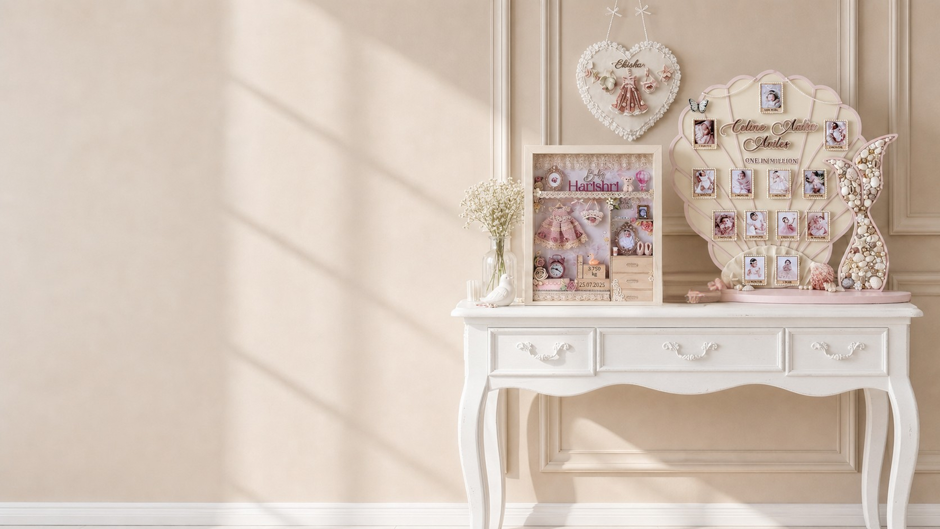 Cream-toned styled interior with a white console table displaying a personalized baby shadow box keepsake frame and a shell-shaped milestone photo board, with a heart wall hanging above