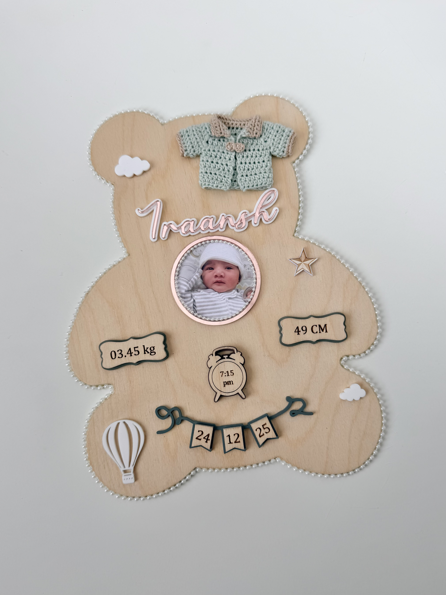 Natural wood teddy-bear-shaped birth plaque with pearl edging, a baby photo, the baby's name, a crocheted cardigan, and birth-weight, length, and time details