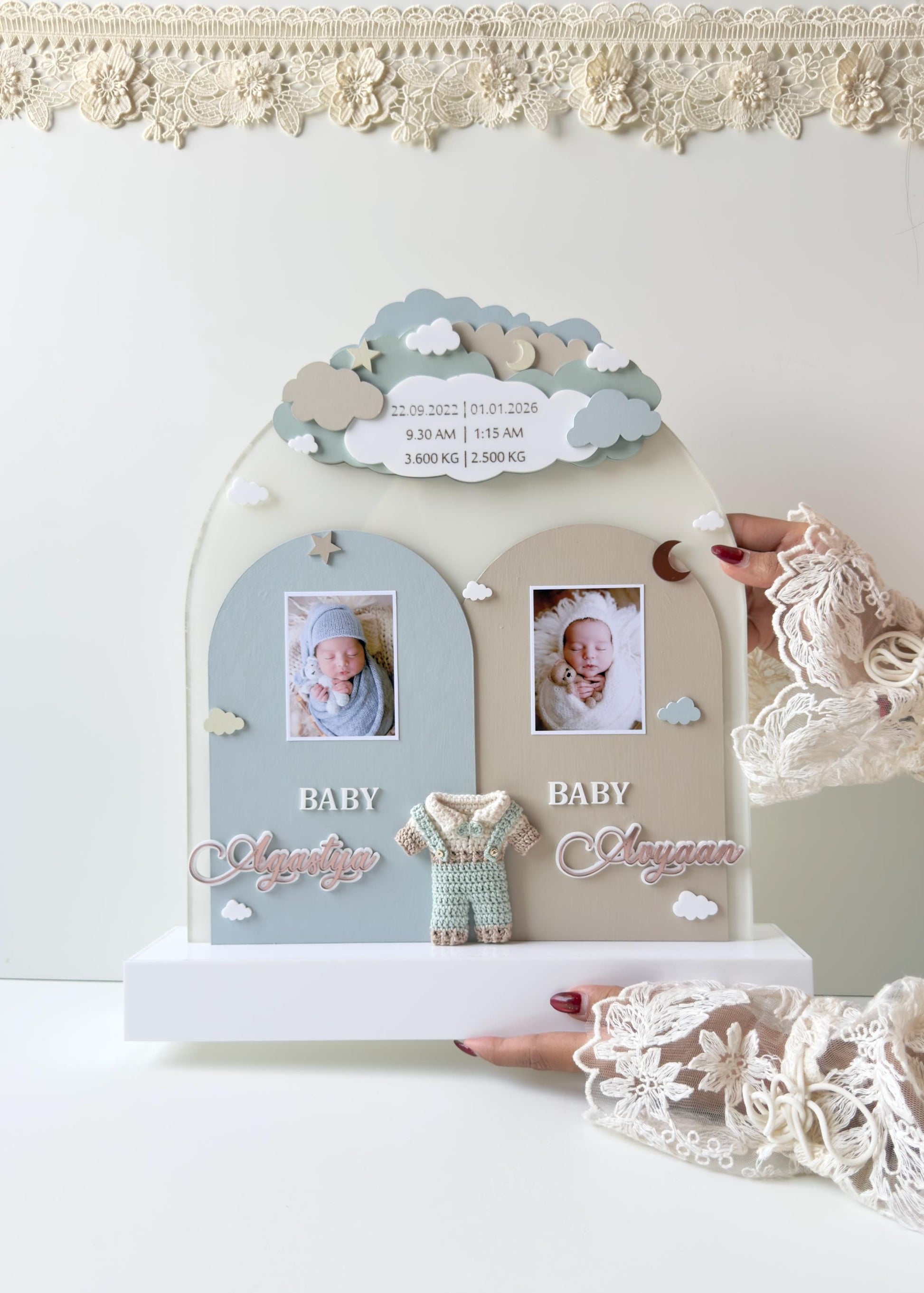 Double-arch cloud-topped wooden keepsake board for twins, with two baby photos, both names, a crocheted romper, and birth stats for each baby