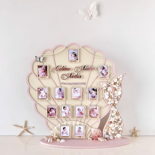 Mermaid-tail-shaped nursery keepsake board with thirteen photo frames, a shell-encrusted tail, and starfish and seashell accents on a stand