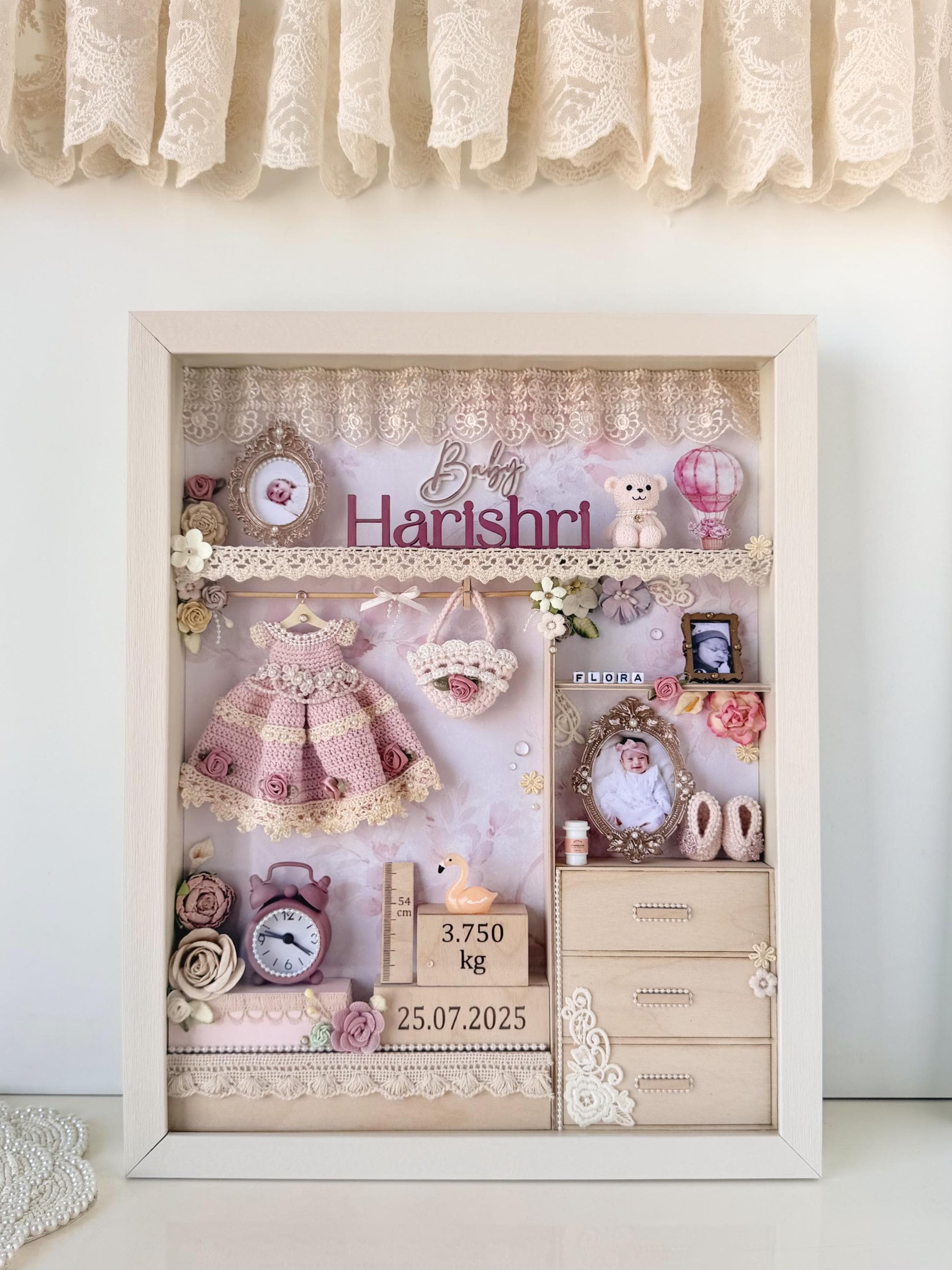 Shabby-chic nursery shadow box with a crocheted dress and bag, a miniature dresser, teddy bear, alarm clock, and wooden birth-weight and date blocks