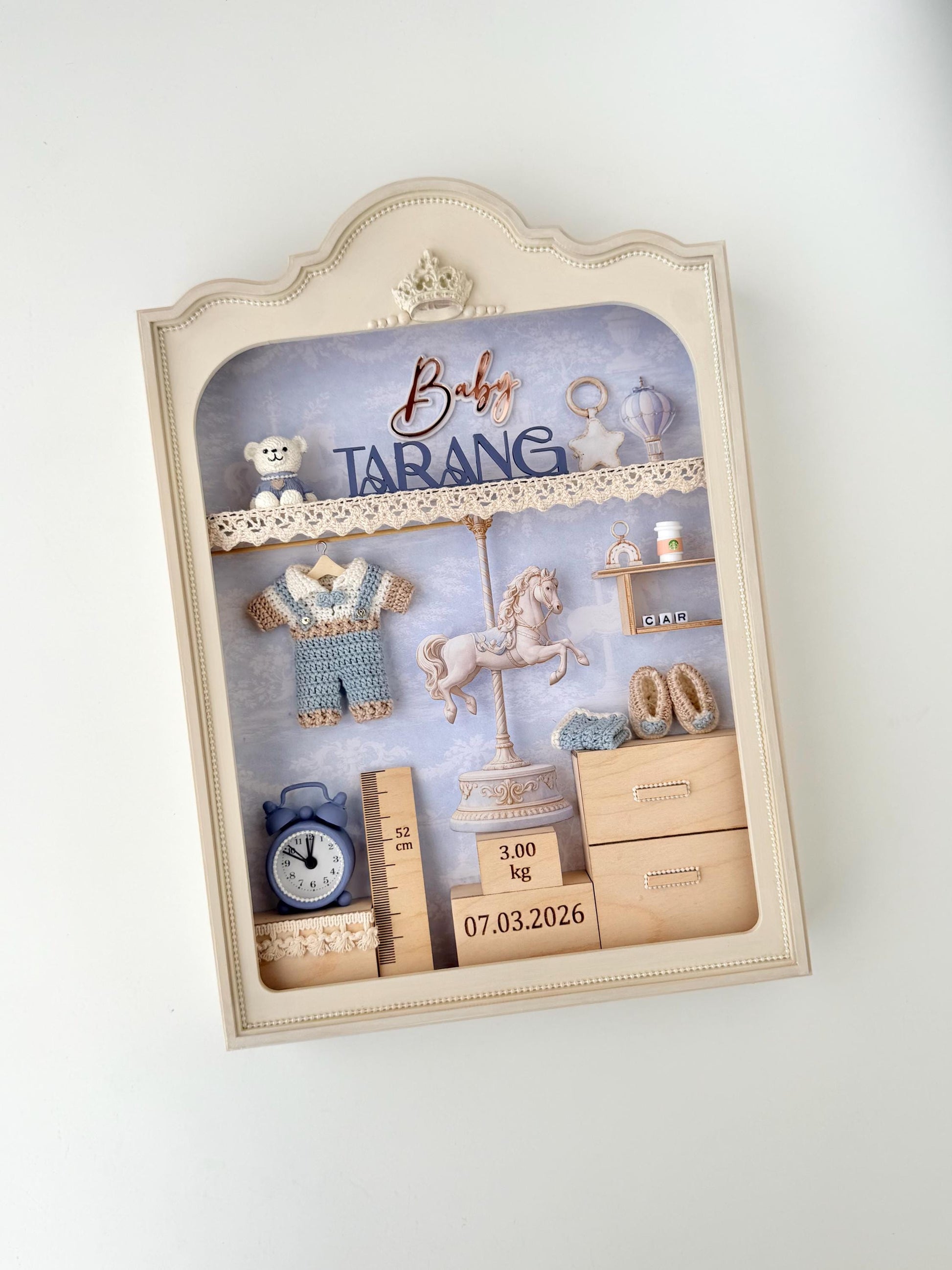 Vintage-style nursery shadow box with a carousel horse figure, crocheted romper, teddy bear, alarm clock, height ruler, and wooden birth-weight and date blocks