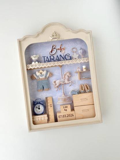 Vintage-style nursery shadow box with a carousel horse figure, crocheted romper, teddy bear, alarm clock, height ruler, and wooden birth-weight and date blocks
