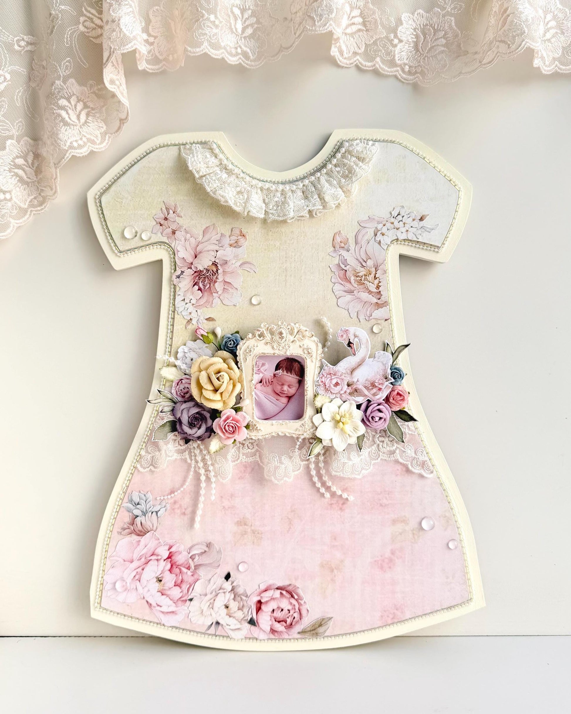 Dress-shaped wooden keepsake frame with pink paper florals, lace trim, an oval baby photo, and a paper swan accent