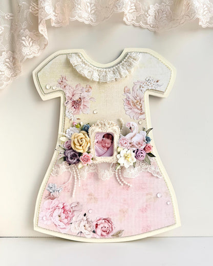 Dress-shaped wooden keepsake frame with pink paper florals, lace trim, an oval baby photo, and a paper swan accent