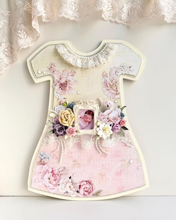 Dress-shaped wooden keepsake frame with pink paper florals, lace trim, an oval baby photo, and a paper swan accent